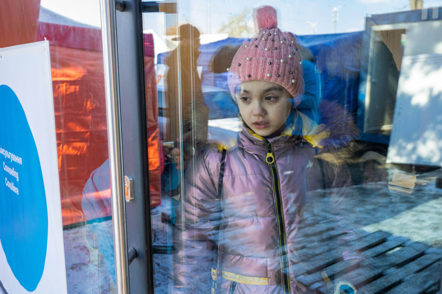child wearing a warm coat and bobble hat standing inside a blue dot hub