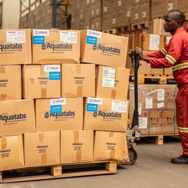 Boxes of Aquatabs water purification tablets are moved around a warehouse.