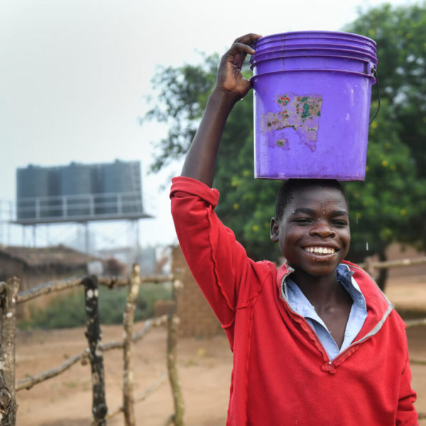 Steven carries water from a solar powered water tap in Malawi