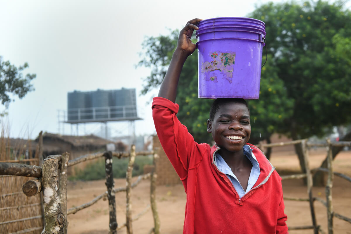 Steven carries water from a solar powered water tap in Malawi