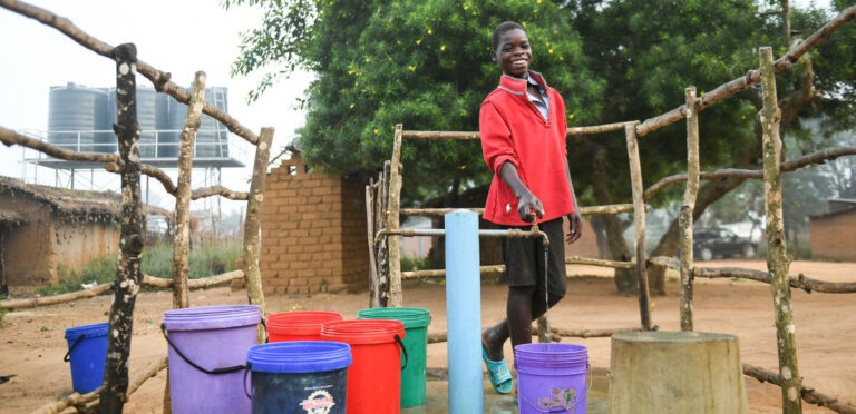 Steven stands behind a clean water pump and jugs for collection.