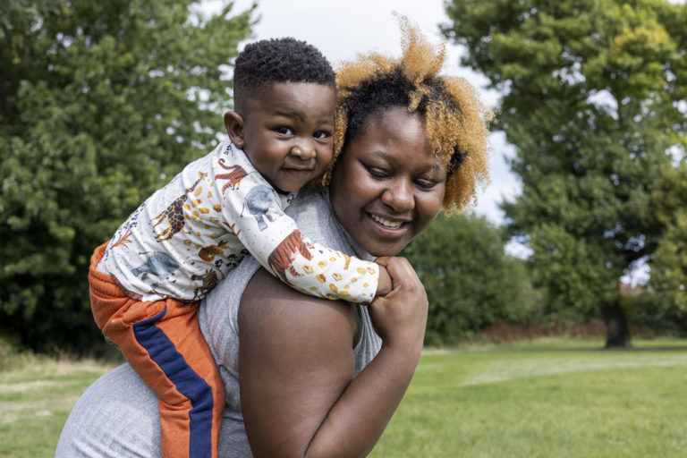 Andrea has her son on her back, surrounded by grass, as they smile.