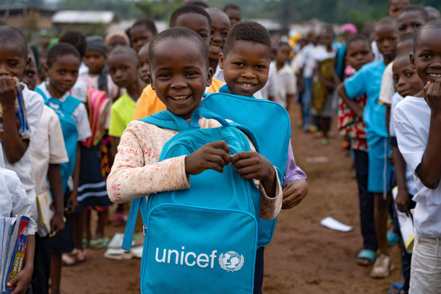 Young boy looking into the camera, smiling and holding a UNICEF bag