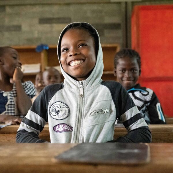 A girl sits behind her desk and smiles among her classmates.