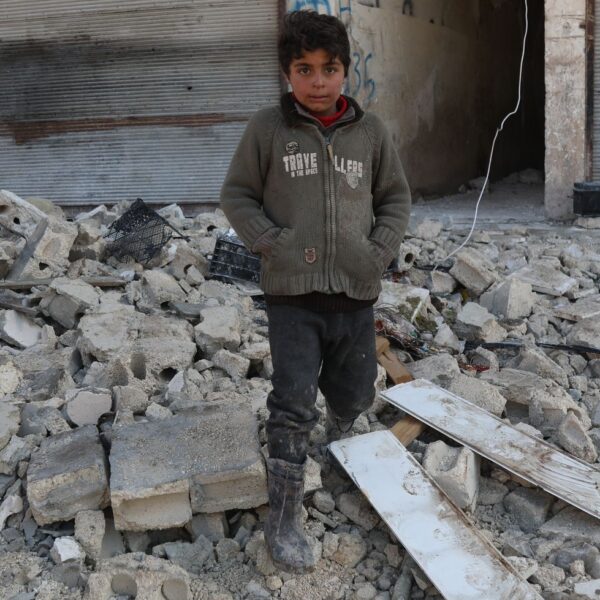 child stands amid the rubble of a collapsed building in Syria after the Turkyie-Syria earthquakes