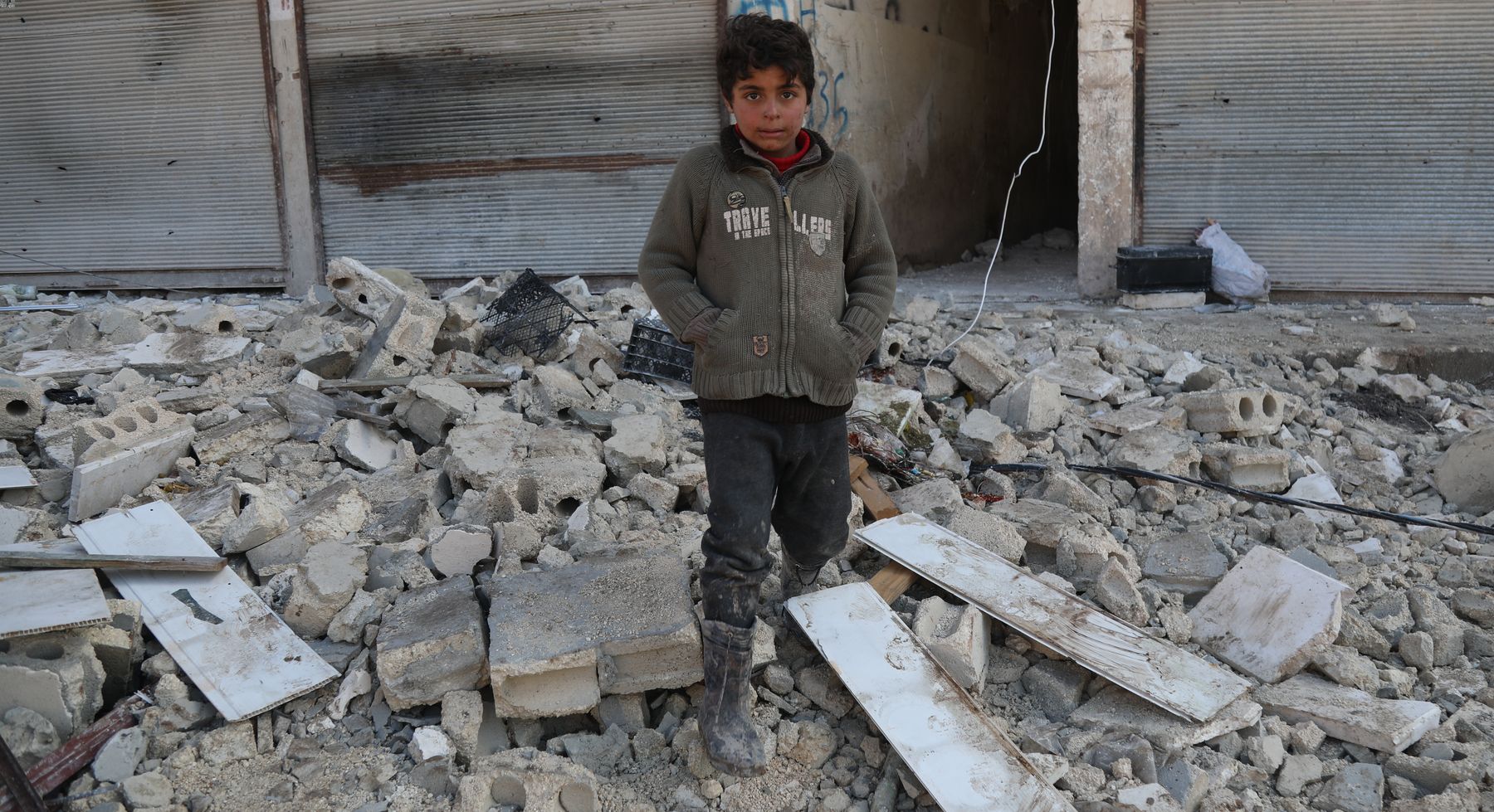 child stands amid the rubble of a collapsed building in Syria after the Turkyie-Syria earthquakes