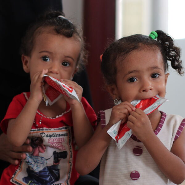 Two girls bite into packets of therapeutic food