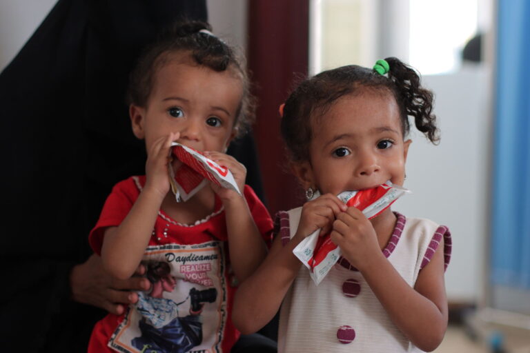 Two girls bite into packets of therapeutic food