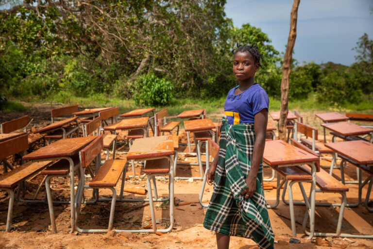 Mozambique, 2022. 13-year-old Mariano stands in front of her school, which was destroyed by Cyclone Gombe. The cyclone caused widespread flooding, forcing thousands of people from their homes.