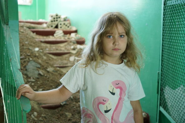 8-year-old Nastya stands amidst rubble in her damaged school in Buzova, Ukraine.