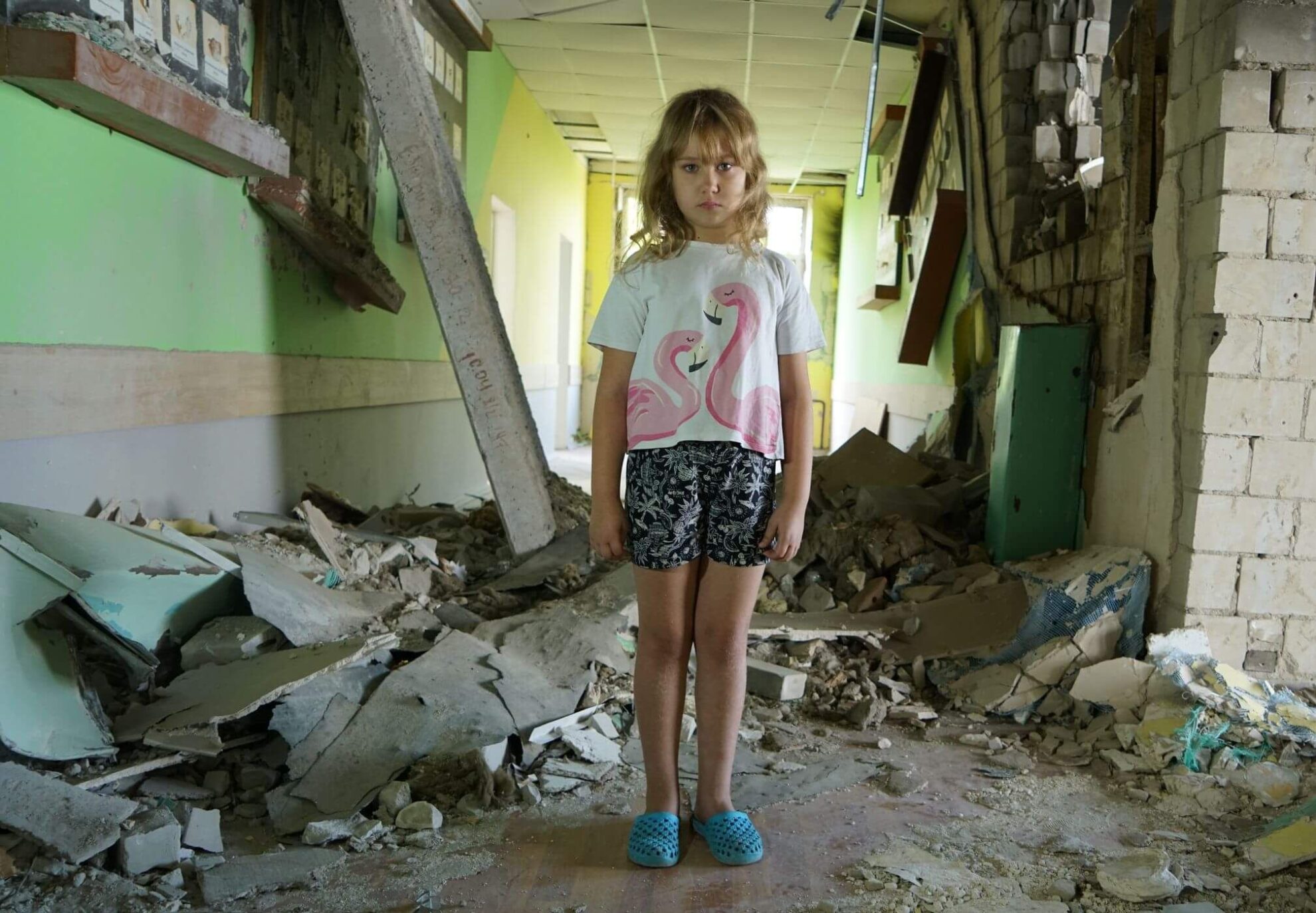 8-year-old Nastya stands amidst rubble in her damaged school in Buzova, Ukraine.