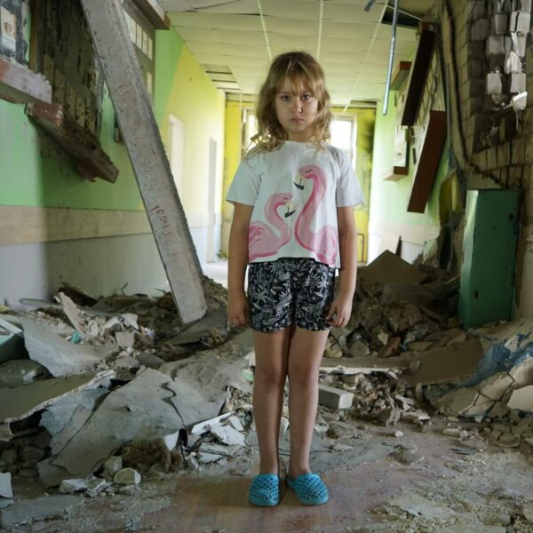 8-year-old Nastya stands amidst rubble in her damaged school in Buzova, Ukraine.