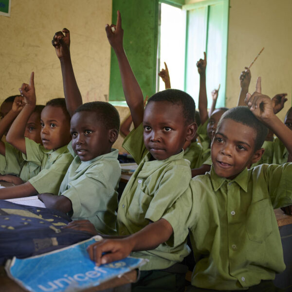 Children raising their hands to answer a question from a teacher.