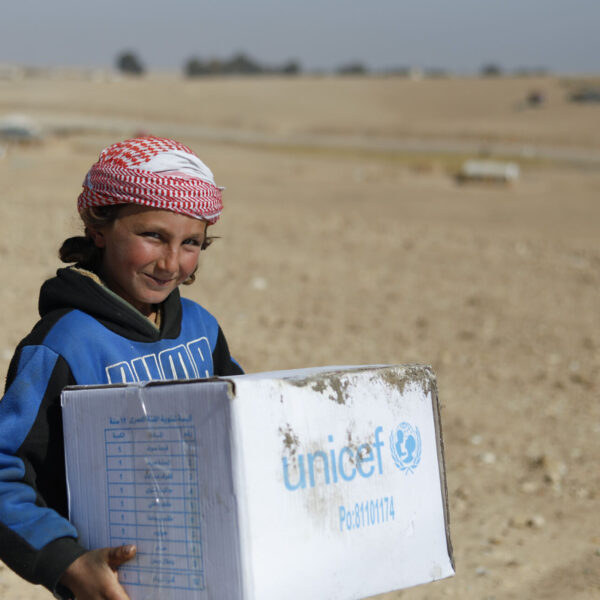 A little Syrian child is happily helping his mother to hold winter clothes’ boxes distributed by UNICEF in Eastern Raqqa rural, Salhabiya informal settlement on 13 February 2022.