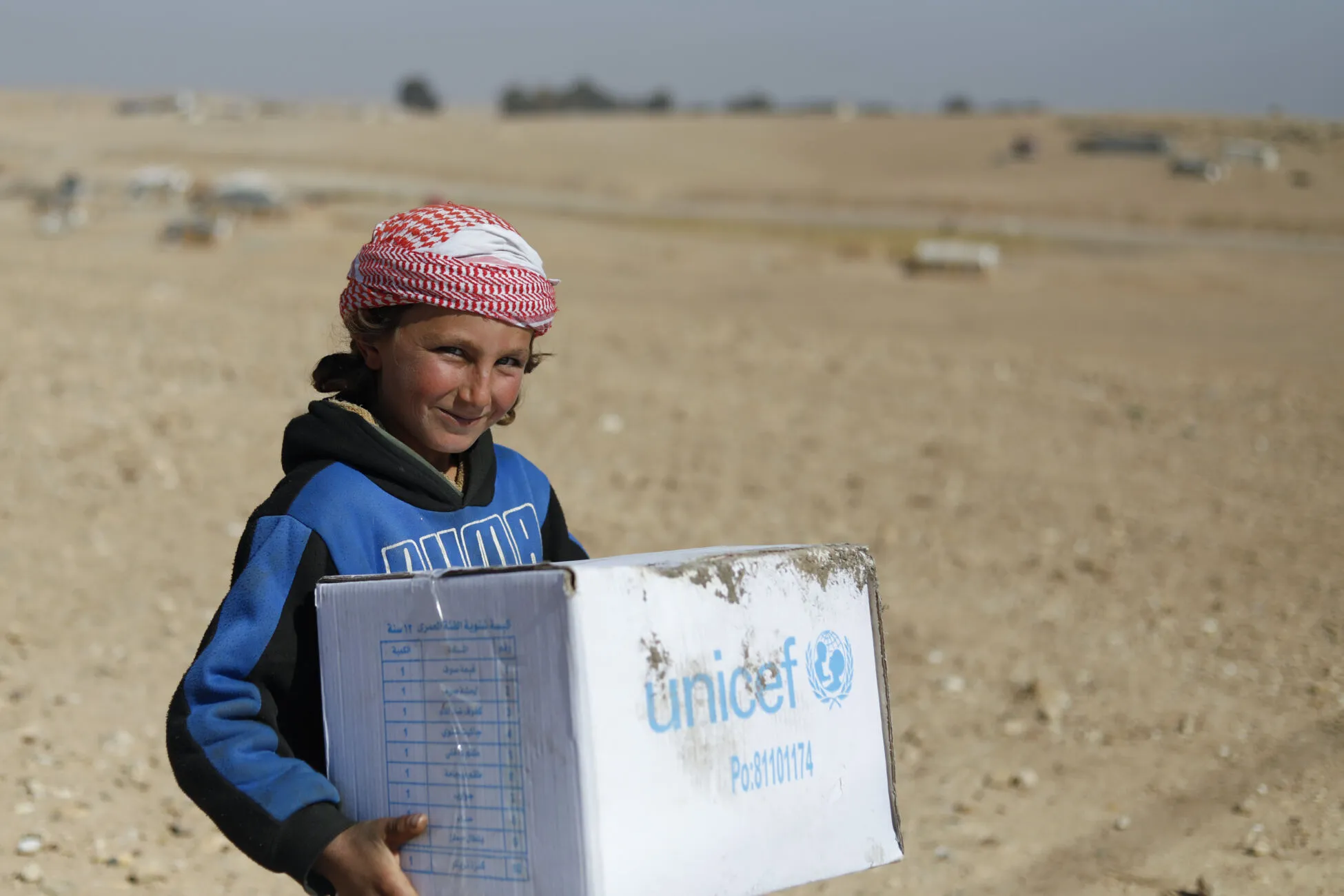 A little Syrian child is happily helping his mother to hold winter clothes’ boxes distributed by UNICEF in Eastern Raqqa rural, Salhabiya informal settlement on 13 February 2022.