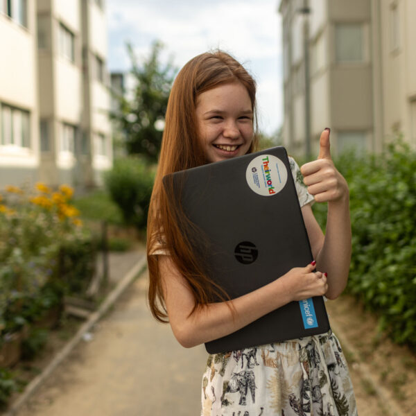 Girl smiling and holding a laptop in her arms.
