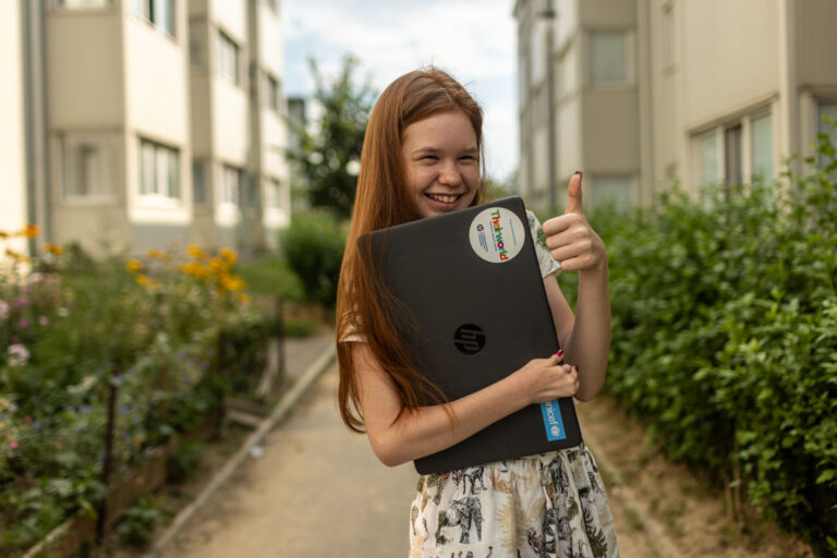 Girl smiling and holding a laptop in her arms.