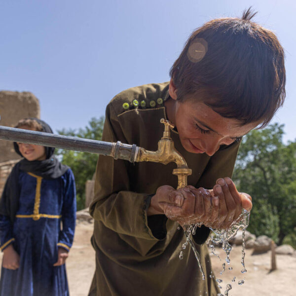 A 9 years old washes his hands at a new water tap at his home, with his 6 years old sister, behind him.