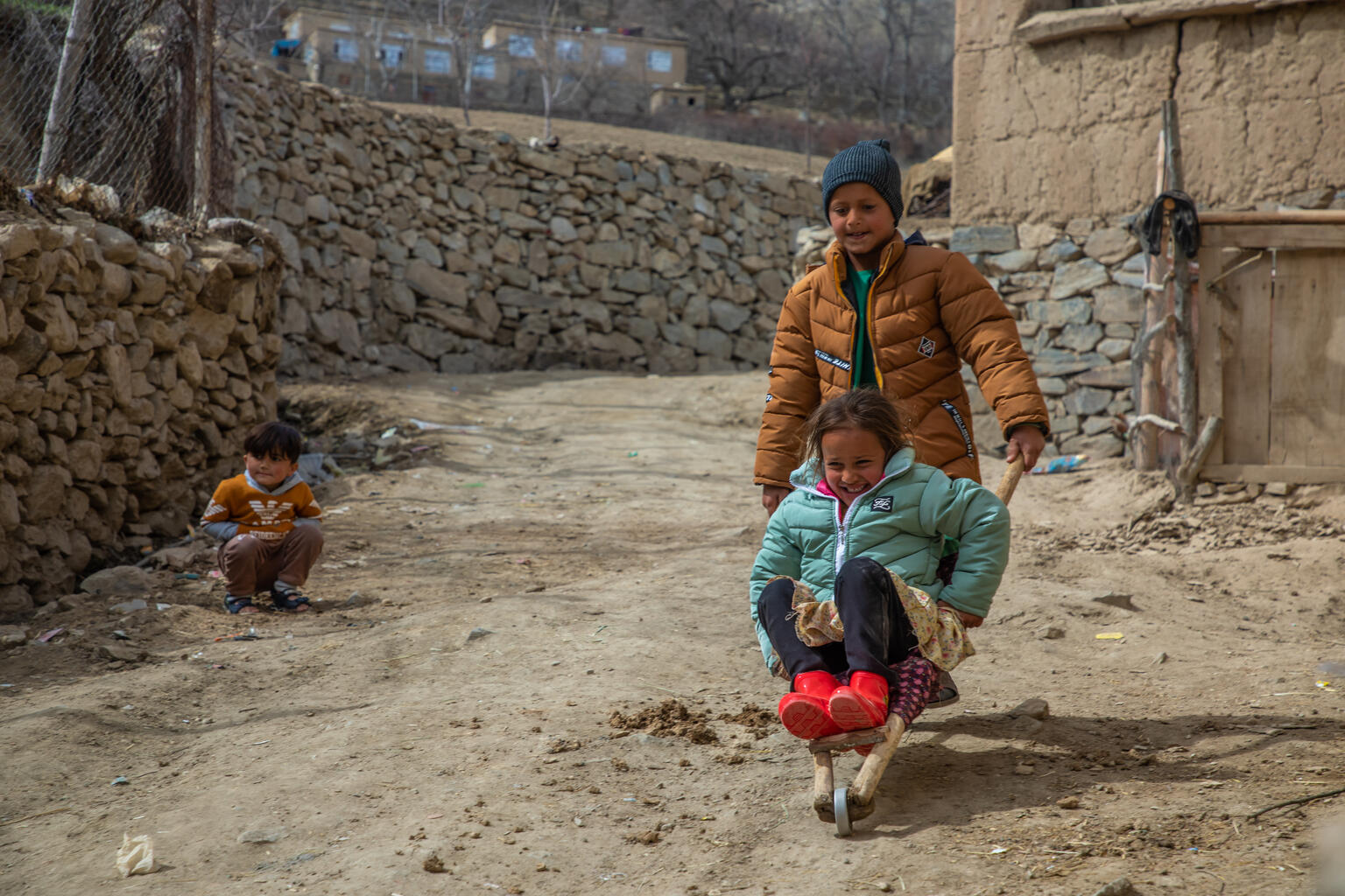 In Panjshir, Afghanistan, an older boy pushes a younger girl on a trolley, both are smiling.