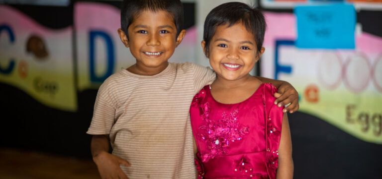 Two girls from a UNICEF-funded day care center in Bangladesh smile at the camera with their arms around each other
