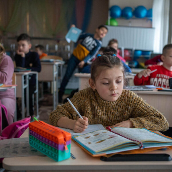 A 10-year-old girl is seated at a desk in her kindergarten class.