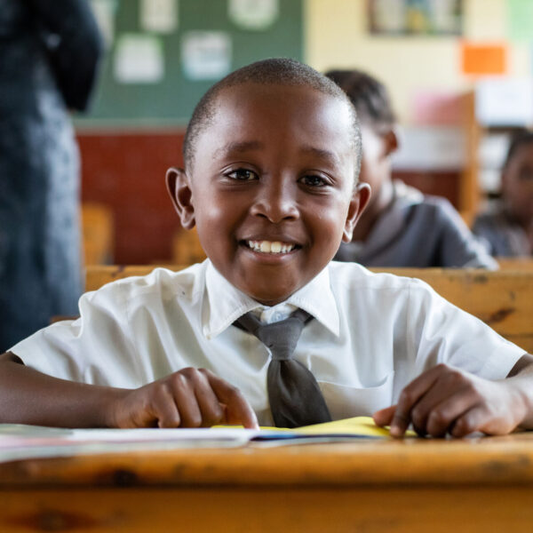 A schoolchild sits behind a desk and smiles.