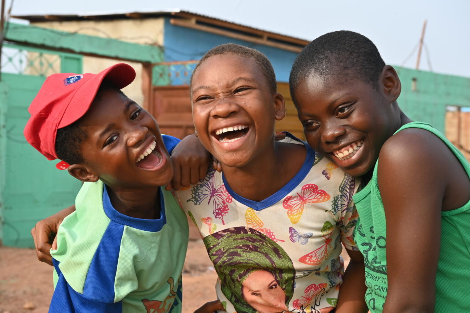 Three boys smiling and laughing with their arms around one another.