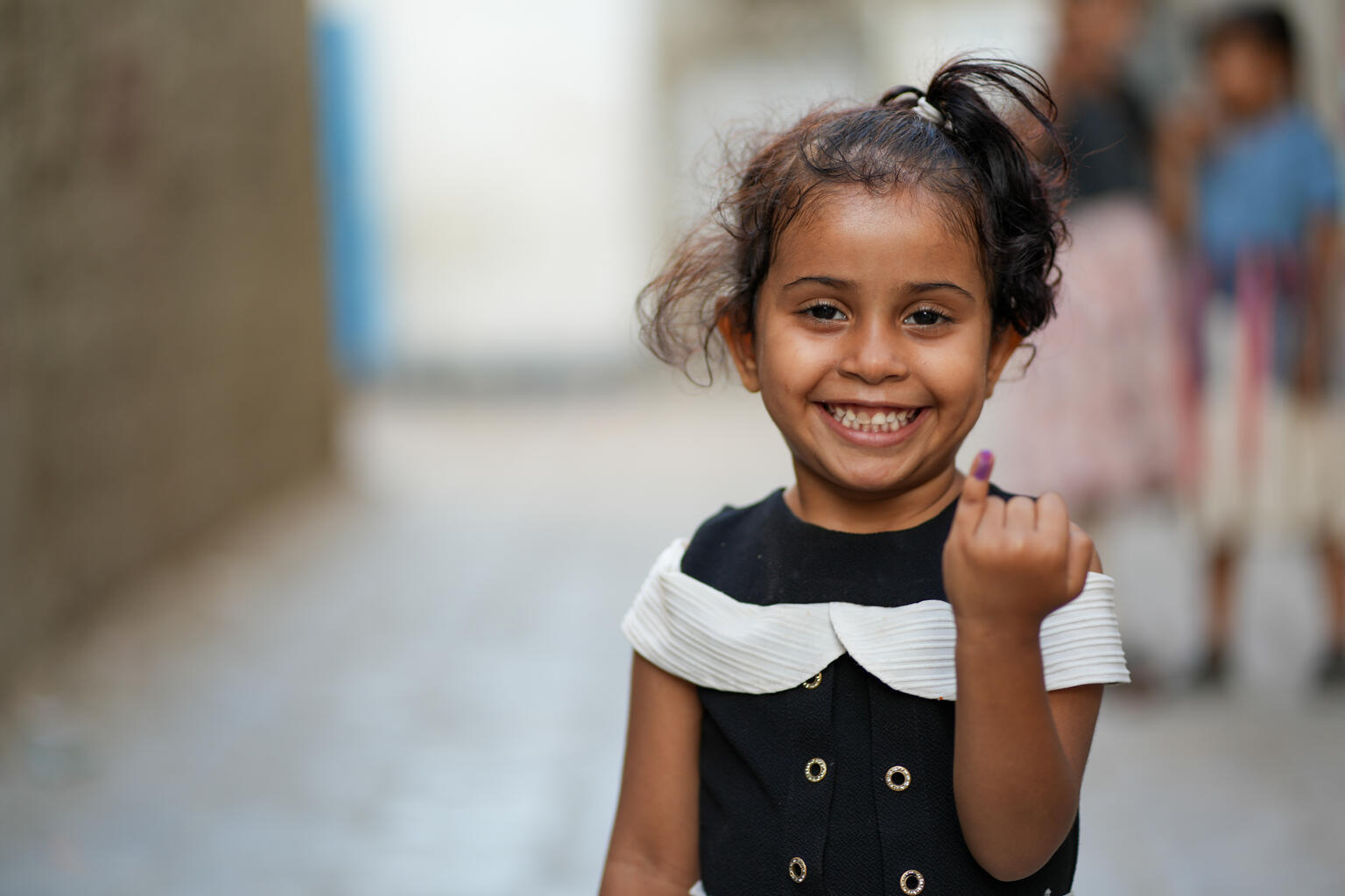 A young girl holds up her little finger, which has been marked to indicate that she has received her vaccines.