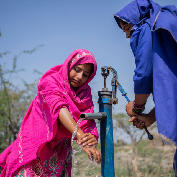 Two girls in brightly coloured clothing pump clean water in Pakistan.