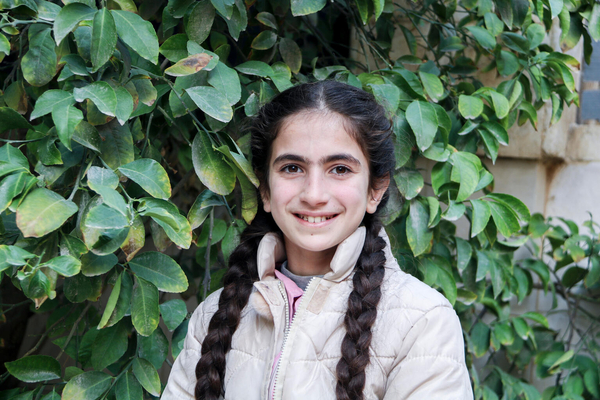 12-year-old Asma smiles outside a child-friendly safe space.