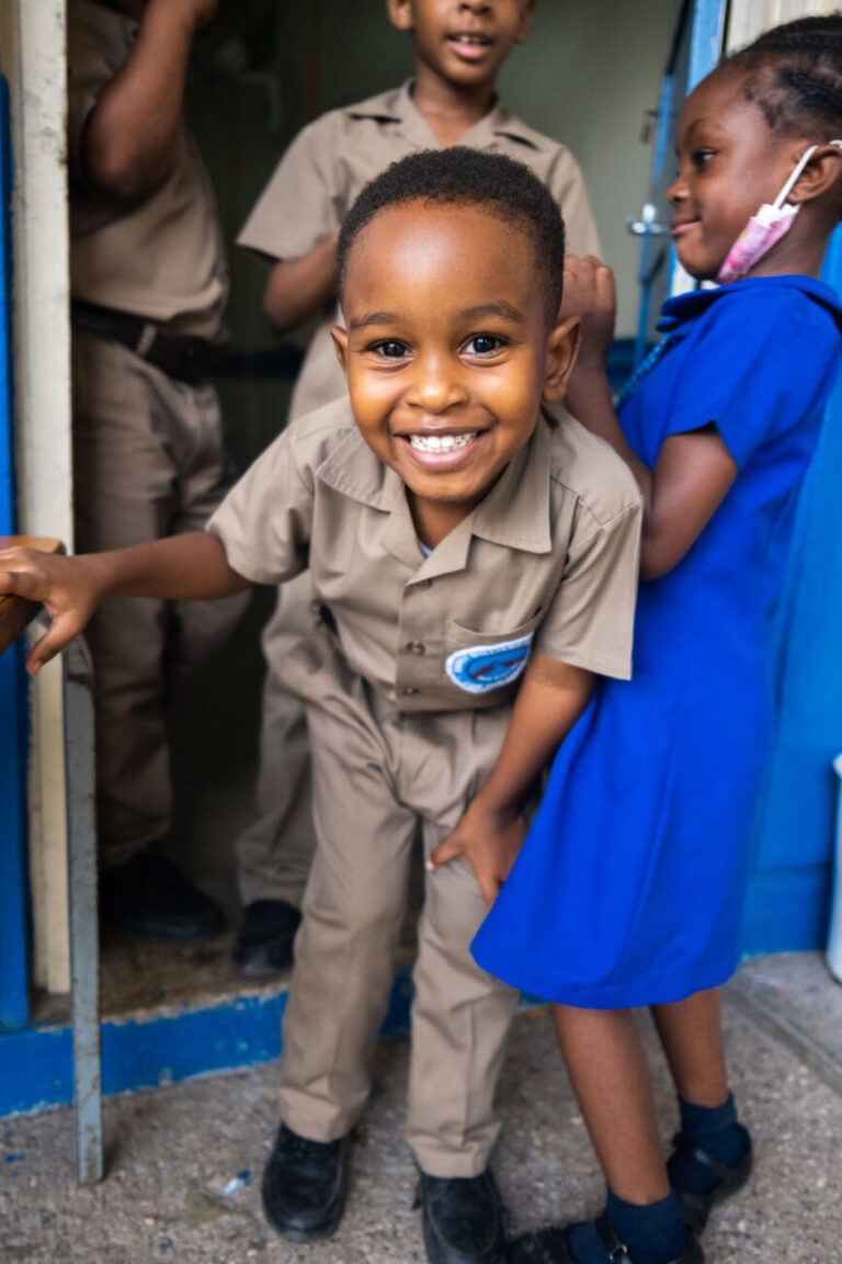 Ari stands in the doorway smiling in his school uniform, surrounded by his peers.
