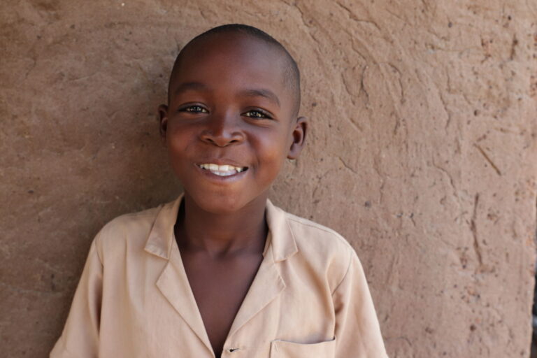 8-year-old Abasse smiles in front of his family home.