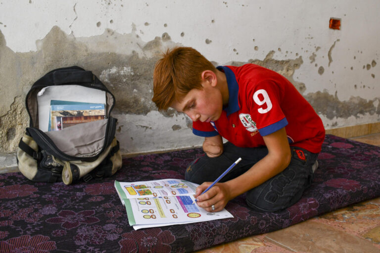 Abdulrahman kneels on the floor and concentrates on his homework.