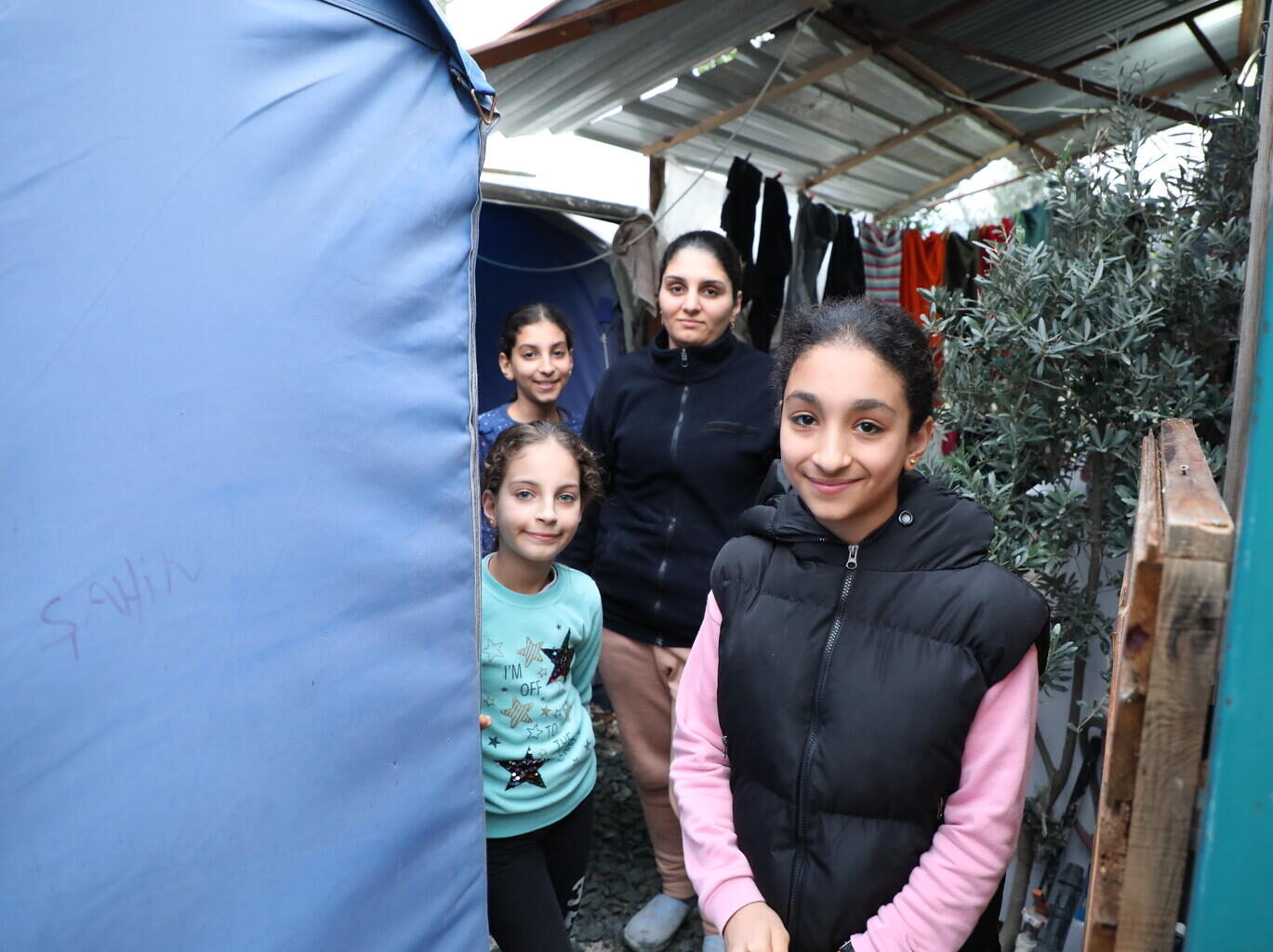 14-year-old Ela stands in the doorway of her temporary accommodation. Her family are in the background.