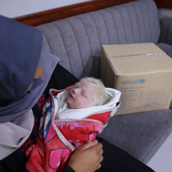 Dareen holds her baby Khaled in a pink blanket as she receives a box of essential baby supplies made possible by our Gaza appeal.