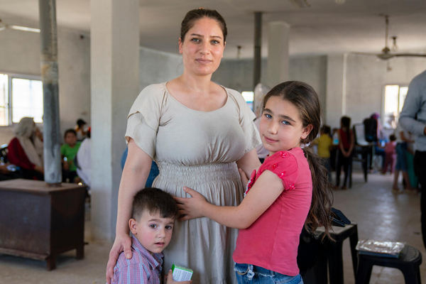 A pregnant mother, with her two children wait together in a mobile clinic in Syria.