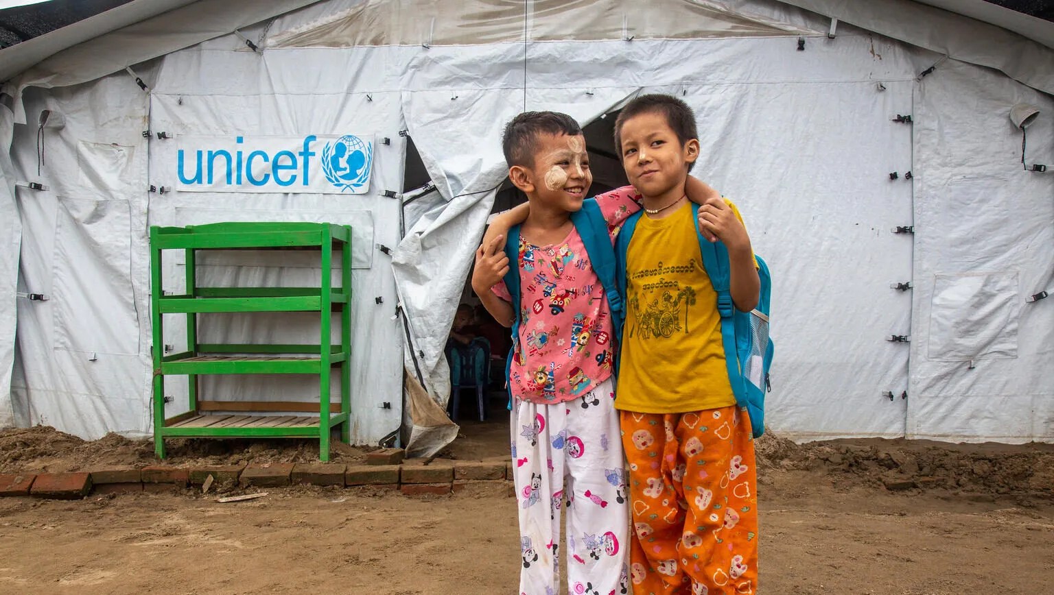 Myat Min Paing, 7 (left), and Kaung Htet Aung, 9 (right), stand together in front of a UNICEF-supported temporary learning shelter at a monastic education centre in Sagaing Region.