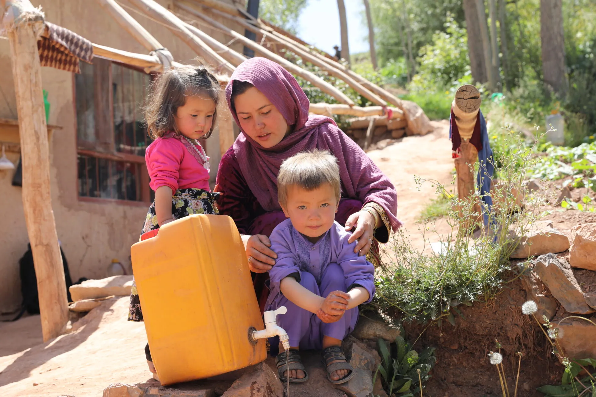 Mother Nikbakht washes her young son’s hands with soap outside their home in Bamyan, Afghanistan, using water from a yellow container.