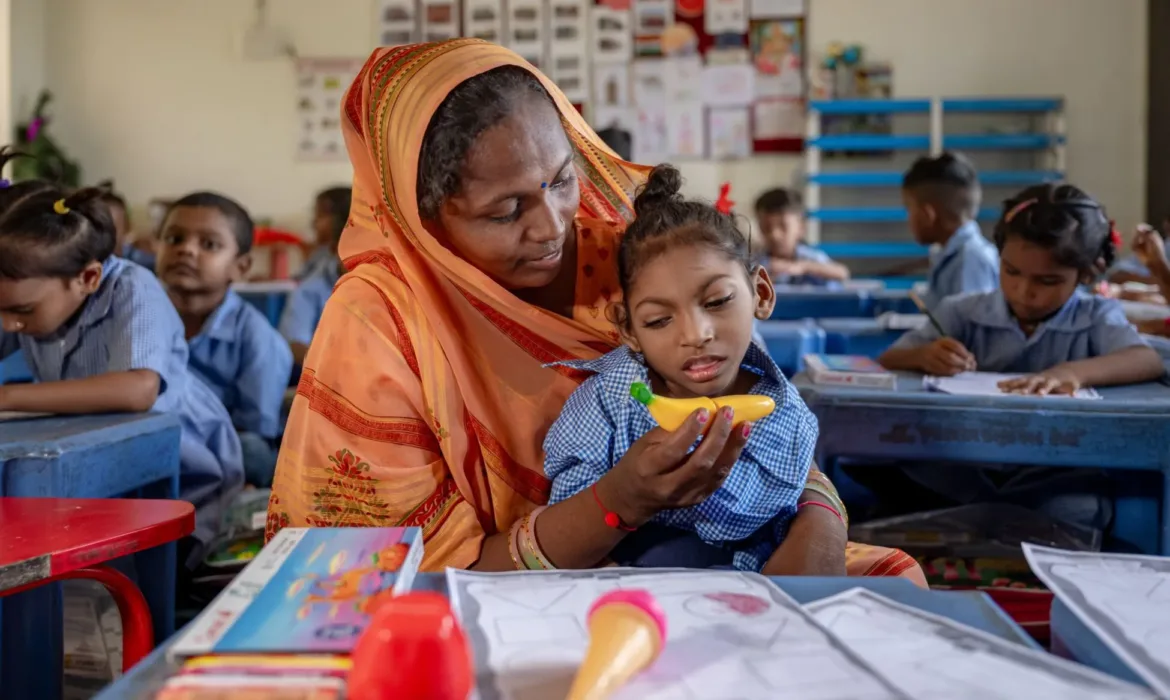 A 6 year old boy with physical challenges sits in a classroom, with his mother supporting him to learn. ©UNICEF/Panjwani