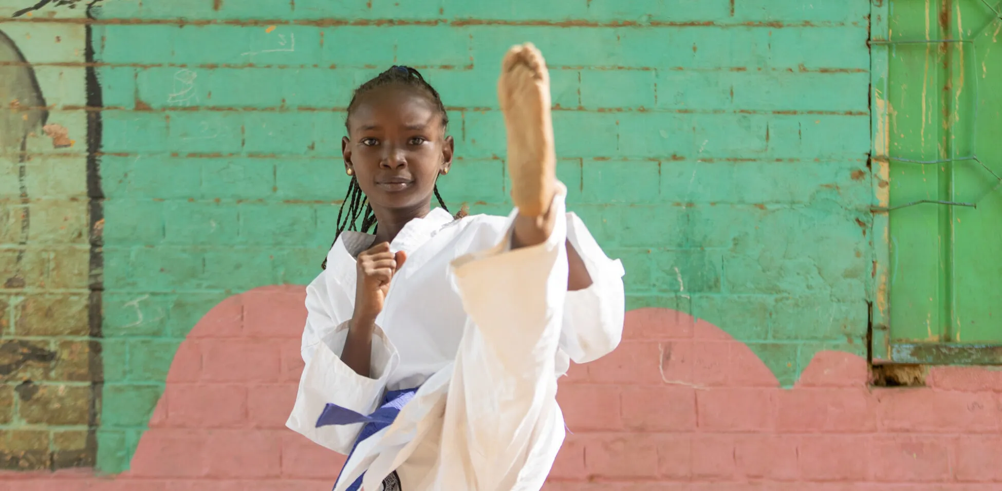 Girl in a karate uniform kicking with one leg in the air.