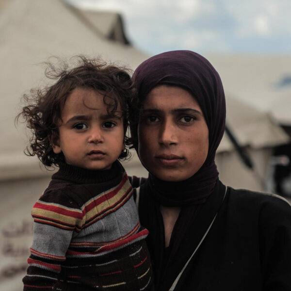 Maysaa, a mother of 5, looks solemn while holding her daughter outside their makeshift tent.