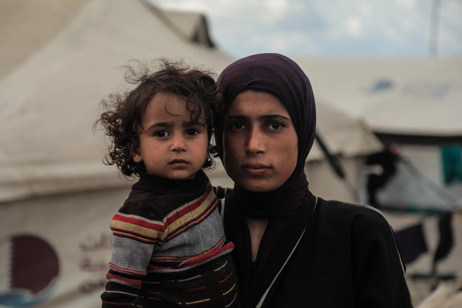 Maysaa, a mother of 5, looks solemn while holding her daughter outside their makeshift tent.