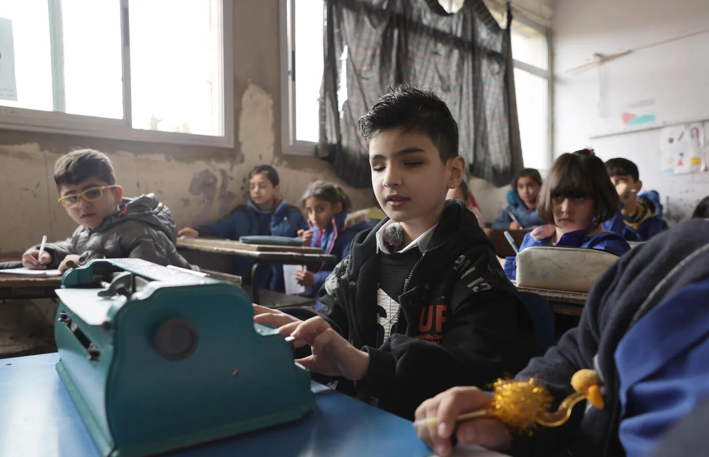Eight‑year‑old Youssef sitting in a classroom using his Braille machine.