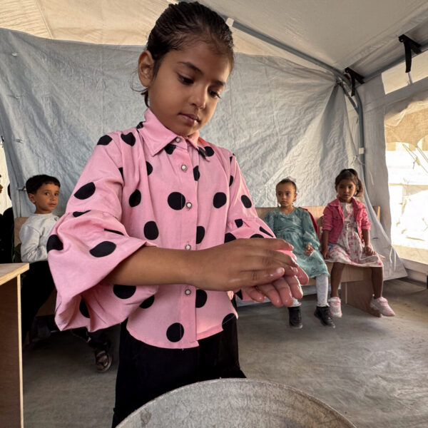 Palestinian little girl in bright pink blouse washing her hands diligently.
