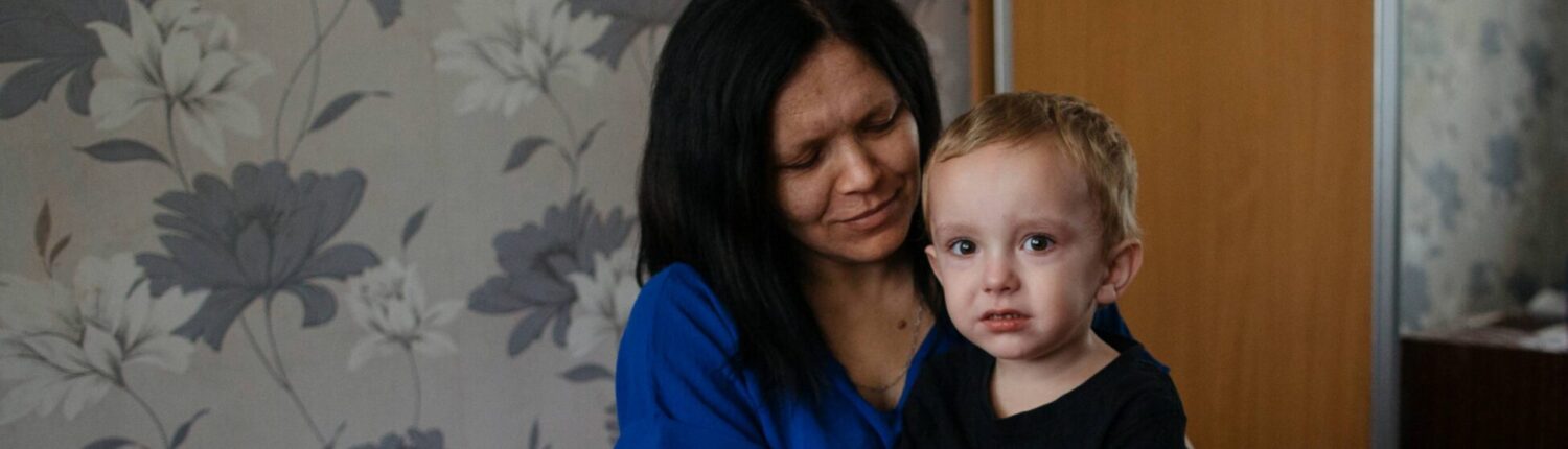 Ganna sits on a bed holding her youngest son inside the communal room where their family is temporarily living in Kherson, southern Ukraine.