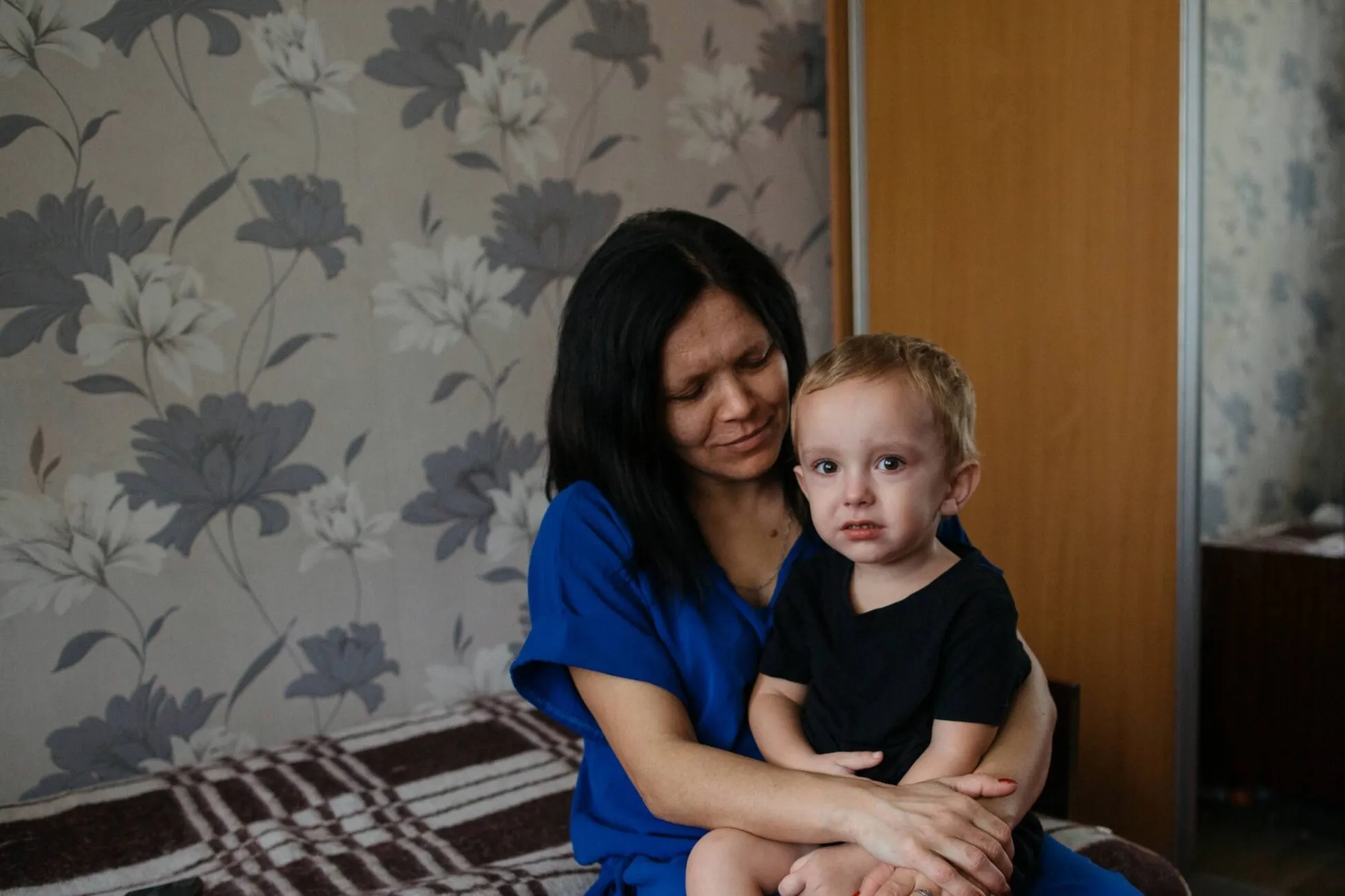 Ganna sits on a bed holding her youngest son inside the communal room where their family is temporarily living in Kherson, southern Ukraine.