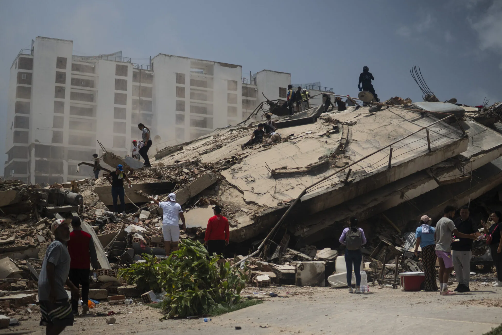 People standing in front of collapsed building after earthquakes in Venezuela.