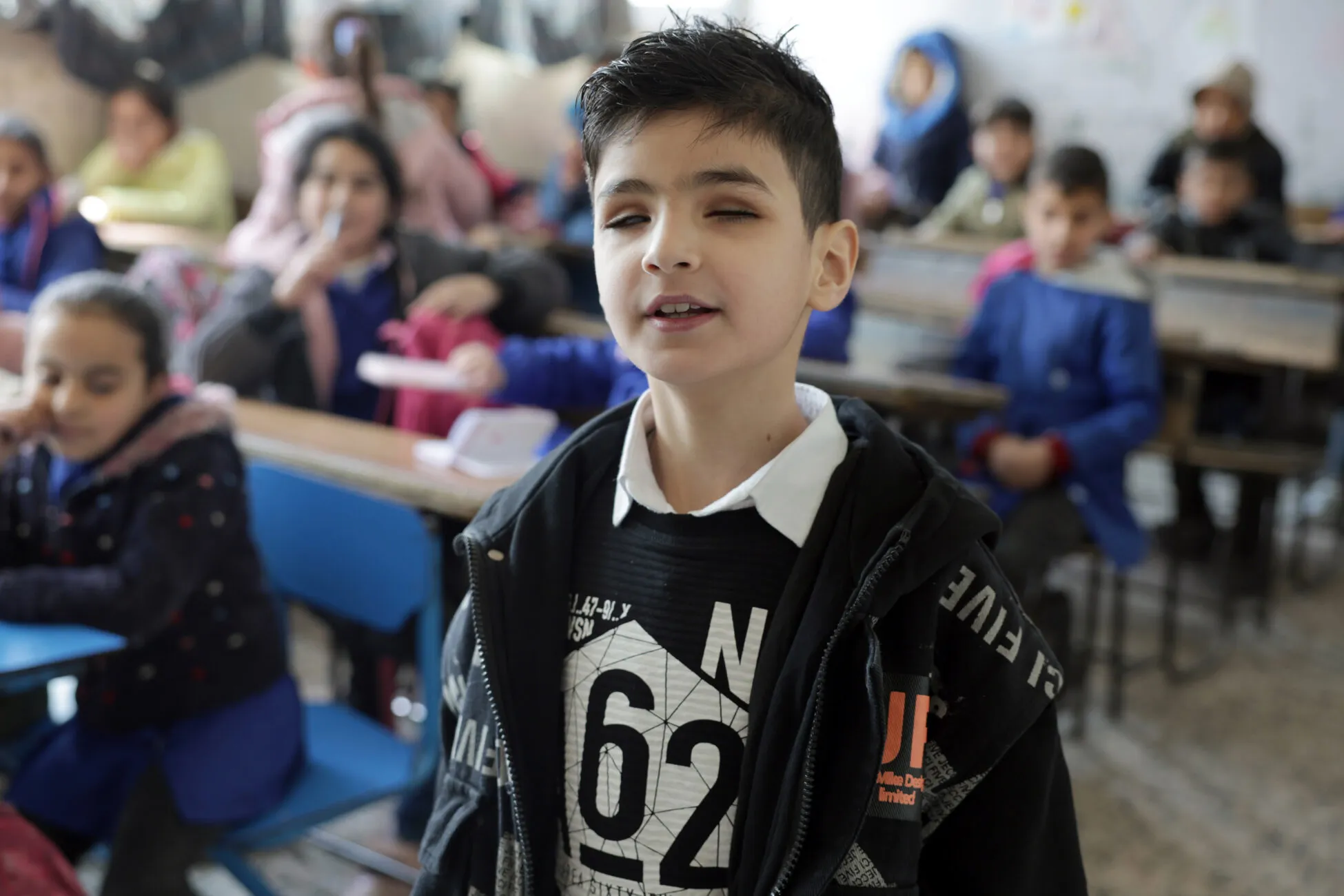 Eight-year-old vision impaired Youssef proudly stands in his classroom in Homs, Syria.